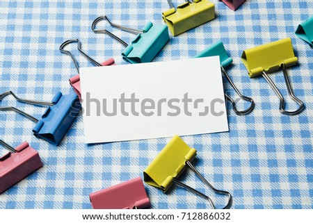 White card on a white-blue checkered background with multi-colored office clothespins