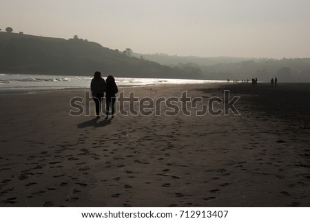 Two females in silhouette in evening sunlight breaking through a misty haze as they walk along a beach