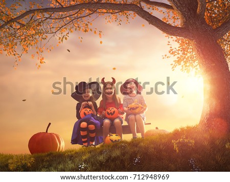 Happy brother and two sisters at Halloween. Funny kids in carnival costumes outdoors. Cheerful children and pumpkins on sunset background.