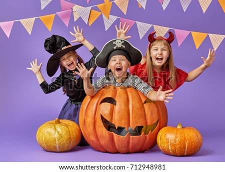 Happy brother and two sisters at Halloween. Funny kids in carnival costumes on background of purple wall. Cheerful children and pumpkins.