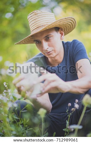 Young man, modern farmer, taking pictures of flowers and meadow with his cell phone