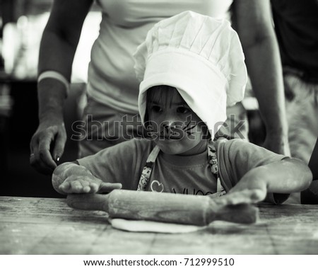 Small child cooking homemade cake, using rolling pin with grandma on kitchen, black and white photo
