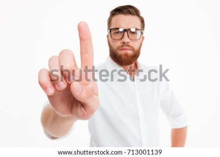 Close up of a young serious bearded man in eyeglasses showing forefinger isolated over white background