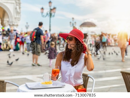Elegant woman with a red hat enjoys an Aperitif on the famous St. Mark's Square in Venice, Italy
