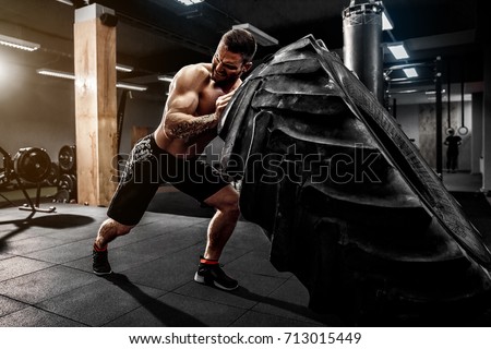 Shirtless man flipping heavy tire at gym Royalty-Free Stock Photo #713015449