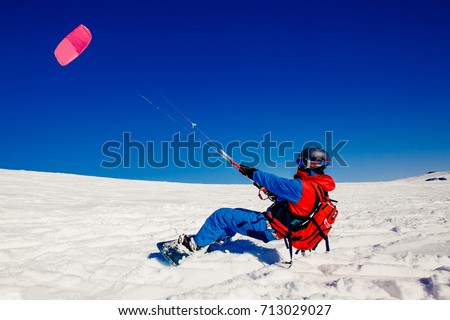 Snowboarder with a kite on fresh snow in the winter in the tundra of Russia against a clear blue sky. Teriberka, Kola Peninsula, Russia. Concept of winter sports snowkite. Royalty-Free Stock Photo #713029027