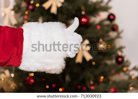 partial view of santa claus showing thumb up against christmas tree