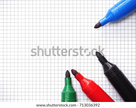 Red, blue, black and green marker pens on blank graph paper sheet background. Top view.