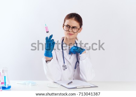 doctor in glasses looks at syringe sits at table on neck stethoscope                               