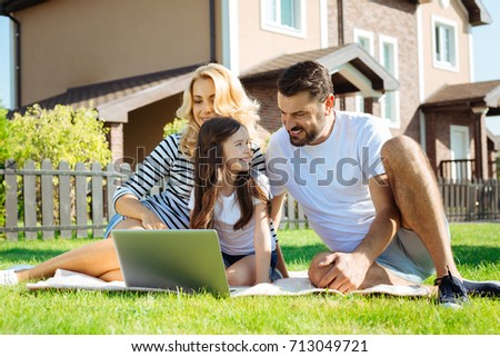 Happy parents watching cartoons with their daughter in yard