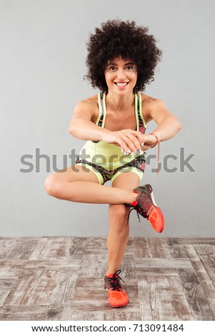 Full length picture of smiling fitness woman doing yoga exercise and looking at the camera over gray background