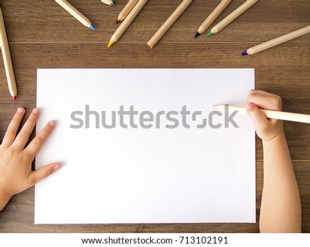 Kid holding pencil over empty white sheet of paper on dark rustic background