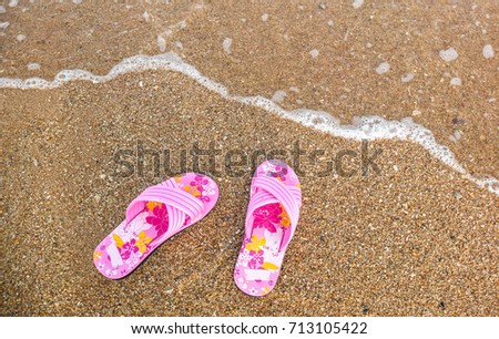 Pink flower sandals on brown sand beach with sea water