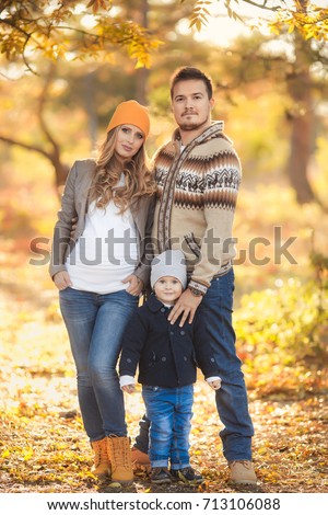 Young happy family have fun and walking in the autumn park. Pregnant woman with husband and little son.