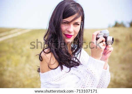 A young amateur photographer with an old camera in the field takes pictures of the neighborhood. Girl with a photo camera on the nature have a good mood on a vacation