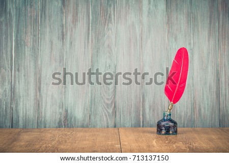 Vintage old red quill pen with inkwell on wooden table front grunge wooden planks wall background. Retro instagram style filtered photo