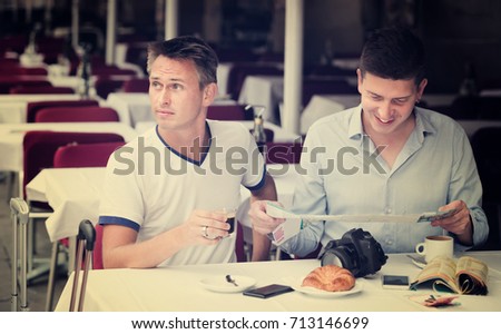 Portrait of smiling men looking at map and drinking coffee with bakery 

