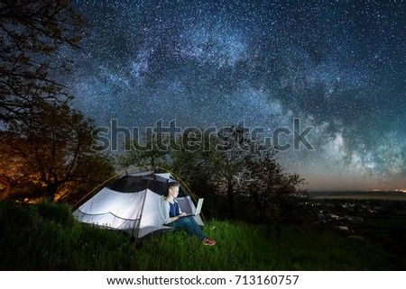 Woman using her laptop in the camping at night. Woman sitting in the tent under beautiful night sky full of stars and milky way. Long exprose