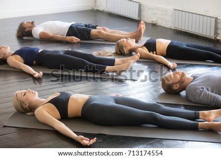 Group of young sporty people practicing yoga lesson with instructor in gym, lying in Dead Body exercise, doing Savasana, Corpse pose, friends relaxing after working out in sport club, studio image  Royalty-Free Stock Photo #713174554