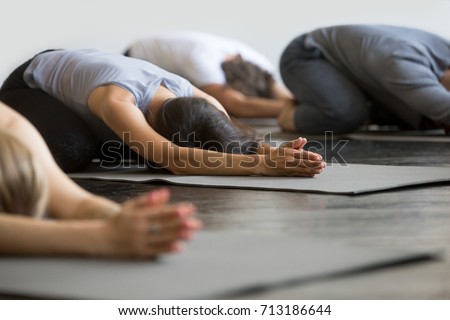 Group of young sporty people practicing yoga lesson with instructor, sitting in Balasana exercise, Child pose, friends working out in club, indoor close up image, studio. Wellbeing, wellness concept  Royalty-Free Stock Photo #713186644
