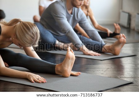 Young sporty people practicing yoga lesson with instructor, sitting in Janu Sirsasana exercise, Head to Knee Forward Bend pose, working out, indoor close up image, studio. Wellbeing, wellness concept  Royalty-Free Stock Photo #713186737