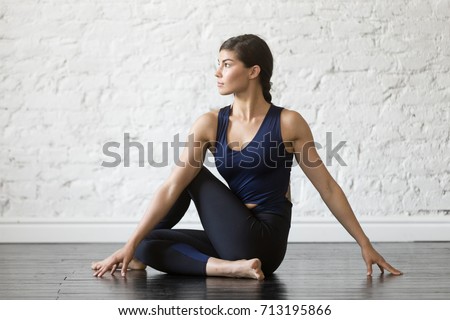 Young attractive woman practicing yoga, sitting in Ardha Matsyendrasana exercise, Half lord of the fishes pose, working out, wearing sportswear, black top, pants, indoor full length, studio background Royalty-Free Stock Photo #713195866