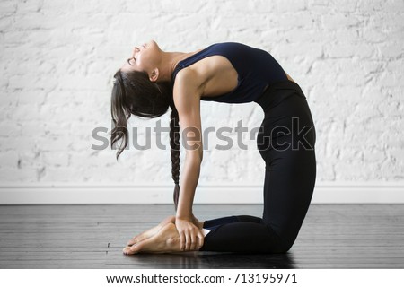 Young attractive woman practicing yoga, stretching in Ustrasana exercise, Camel pose, working out, wearing sportswear, black top and pants, indoor full length, studio background  Royalty-Free Stock Photo #713195971