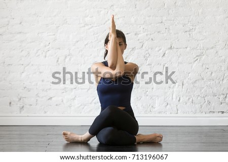 Young attractive woman practicing yoga, sitting in Gomukasana exercise, Cow Face pose, working out, wearing sportswear, black top and pants, indoor full length, studio background  Royalty-Free Stock Photo #713196067