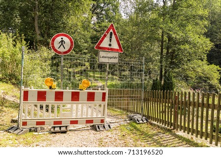 A forest road in Germany was closed. Barriers, eyesight, and two signs warn of the dangers. The passage is also closed to pedestrians and hikers. Remark to the danger sign: Danger to life
