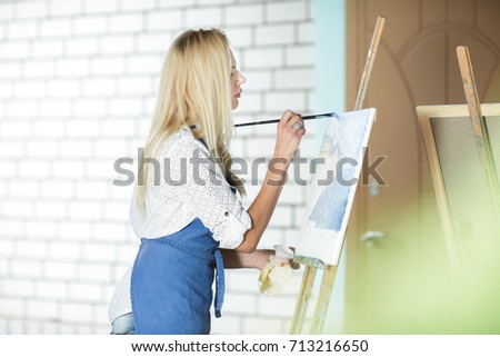 beautiful blonde woman artist with a brush in her hand draws on canvas outdoor.