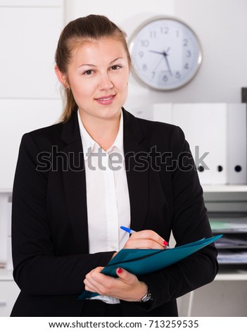 Young manager woman in black suit is signing agreement papers of financial nature at office.
