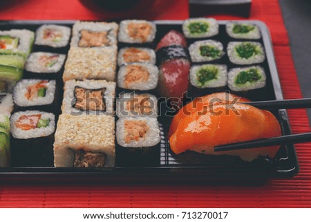 Eating salmon sushi. Japanese food restaurant, sushi maki and roll plate or platter set. Closeup of hand with chopsticks taking roll.