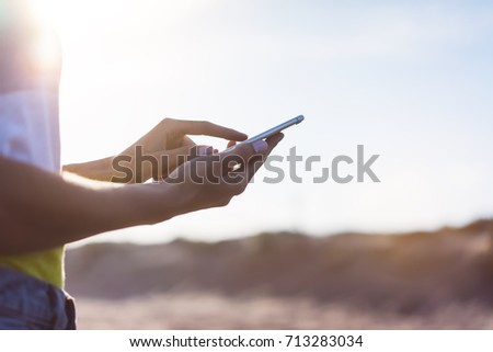 Hipster girl hold on smart phone gadget in sand coastline, mock up  screen. Traveler using in female hand mobile on background beach seascape horizon. Tourist look on blue sun ocean, summer lifestyle 