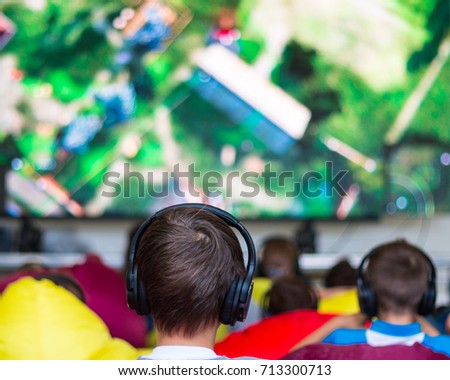 A silent cinema in the open air in the park. Many children in the headphones watch a computer game of a cartoon.