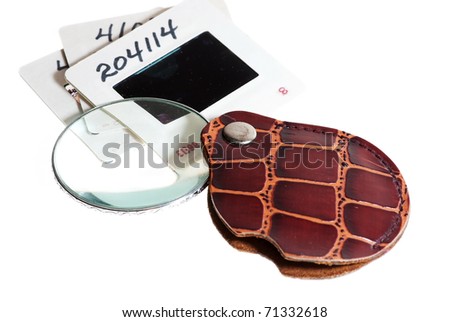 Old photography slides isolated on white being inspected with magnifying glass.
