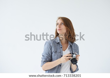 Waist up shot of self-employed female stock photographer working in studio, holding digital camera in her hands, searching for best perspective and angle. People, hobby, profession and occupation.