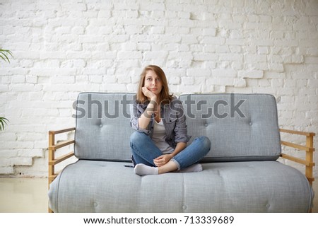 Picture of a tired unkempt woman lying on he couch at home. Girl watch TV new  serial. Sofa relax concept after hard working day. Attentive female in blue jeans and t-shirt watch cooking channel