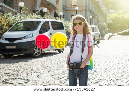 Happy child girl  tourist. With a camera, balloons, a backpack, travels along the street of a European city.