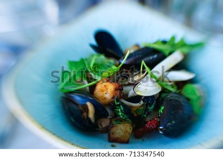Abstract picture of sea food on a blue colored plate. Mix of sea shells, sea fishes and green salad. Great and healthy meals. Place for your text.