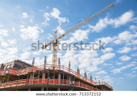 Working crane and safety net on modern office and residential building under construction against cloud blue sky in Downtown New Orleans, Louisiana, US. Red grid prevent objects falling from height.