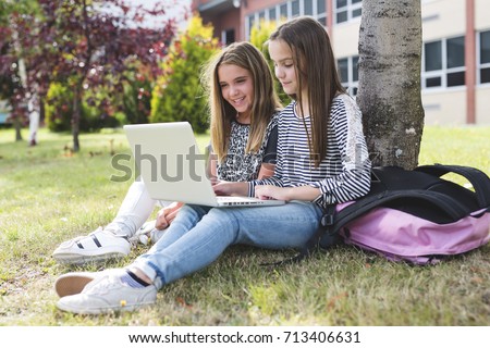 Two smiling female students are sitting on the grass.