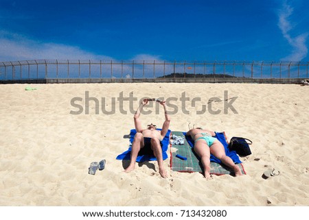 Couple lying on white sand beach relaxing and taking a sunbath in summer at Mai khao beach in front of Phuket international airport , Thailand
