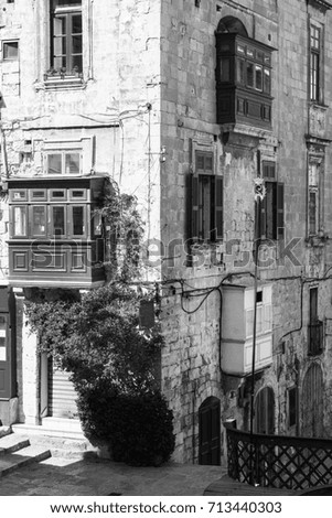 Building with traditional colorful maltese balcony in historical part of Valletta. Red windows decorated with begonville on the facade of a house in Malta. Black and white picture