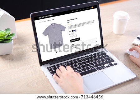 People buying casual shirt on ecommerce website with smart phone on wooden desk Royalty-Free Stock Photo #713446456