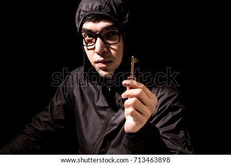 Hacker in a hood holding key on dark background