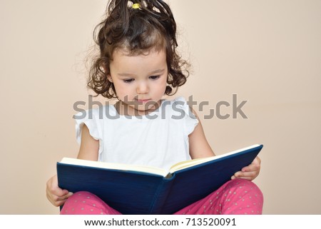 Talented cute three-year-old girl reading a book. Selective focus.
