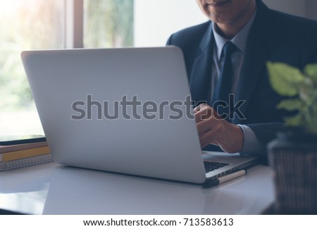 Businessman in black suit working on laptop computer in office near the window, close up