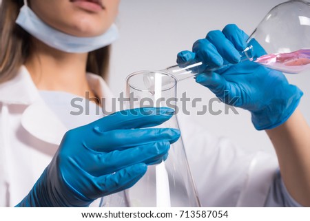 Young woman scientist in blue gloves in a gauze bandage on her face, mixes liquids in flasks