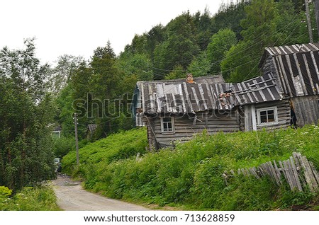 Russia, Kola Peninsula, White Sea coast, Umba pomor settlement. An old, collapsing wooden dwelling house with a lumbering boarded broken fence and a grassy vegetable garden. Old part of the village