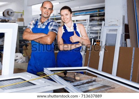 Cheerful positive  man and woman in blue overalls standing with hands crossed at workplace